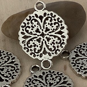 May include: Silver-toned metal charms with a decorative floral design. Each charm has two loops for attaching to jewelry or other crafts.