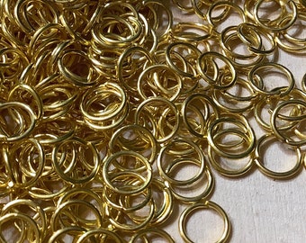 May include: A large pile of gold jump rings. The rings are all the same size and are arranged in a random pattern.