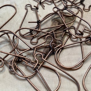 May include: A pile of copper-colored earring hooks, a type of jewelry finding used for making earrings.