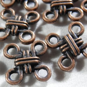 May include: A close-up of several copper-colored metal clasps with a knotted design. Each clasp has four loops, creating a cross shape.