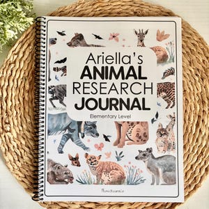 Pode incluir: Um diário com espiral intitulado "Ariella's Animal Research Journal" com ilustrações de vários animais. A capa apresenta um fundo branco com uma variedade de ilustrações de animais, incluindo uma girafa, uma zebra e um leopardo. O diário está em uma esteira tecida.