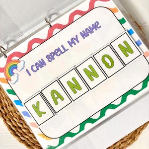 May include: A binder with a colorful educational activity. The page reads "I CAN SPELL MY NAME" with the name "KANNON" spelled out in green letters. The design includes a rainbow and wavy borders in various colors.