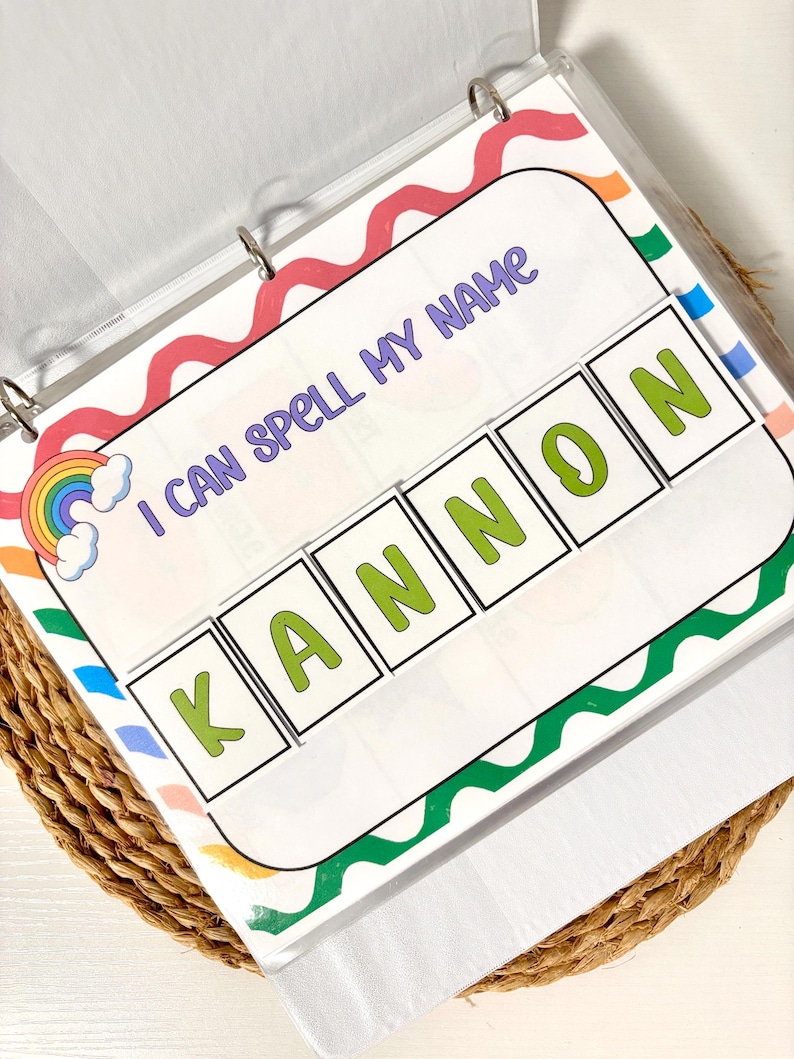May include: A binder with a colorful educational activity. The page reads "I CAN SPELL MY NAME" with the name "KANNON" spelled out in green letters. The design includes a rainbow and wavy borders in various colors.