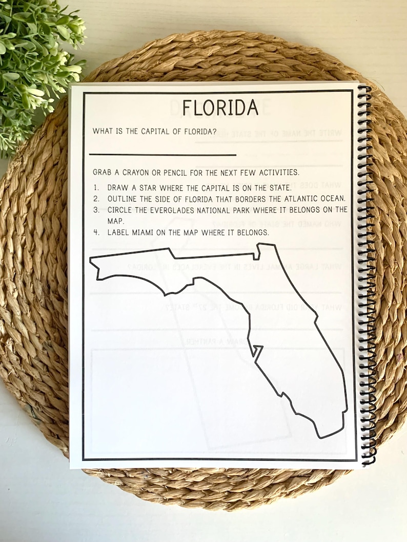 Puede incluir: Una p&aacute;gina de cuaderno con espiral titulada "FLORIDA". La p&aacute;gina incluye preguntas y actividades sobre Florida, como identificar la capital, delinear la frontera estatal y etiquetar Miami en un mapa. El cuaderno est&aacute; sobre una estera tejida.