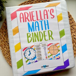 Pode incluir: Uma pasta branca com o texto "Ariella's Math Binder" em letras coloridas. A pasta apresenta materiais educacionais relacionados à matemática, incluindo um relógio, dinheiro e frações. A pasta tem listras diagonais coloridas.