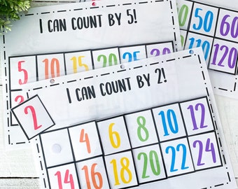 Puede incluir: Tablas educativas para contar con las frases "¡Puedo contar de 2 en 2!", "¡Puedo contar de 5 en 5!" y "¡Puedo contar de 10 en 10!" impresas en negro. Cada tabla tiene una cuadrícula de números coloridos. También se ve un número suelto 2.
