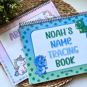 May include: Three spiral-bound name tracing books with unicorn and dinosaur illustrations. The book covers are pastel-colored with the name "Noah" and the words "Name Tracing Book" printed on the front. The books are on a woven mat.