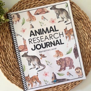 Puede incluir: Un diario de investigación animal de nivel elemental con encuadernación en espiral y portada blanca que presenta ilustraciones en acuarela de varios animales, incluyendo un canguro, un oso, un erizo y un lince, junto a hojas y flores.