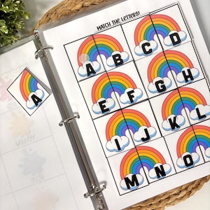 May include: A binder with educational printables. The pages feature colorful rainbow graphics with letters A through O. The text "MATCH THE LETTERS!" is at the top of the page. A rainbow sticker is also visible.