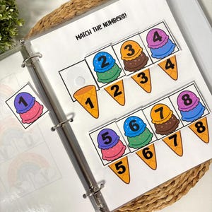 May include: A binder with pages featuring an ice cream-themed number matching game. The text "MATCH THE NUMBERS!" is at the top. Colorful ice cream scoops with numbers 1-8 are paired with matching cone shapes. The binder is on a woven mat.