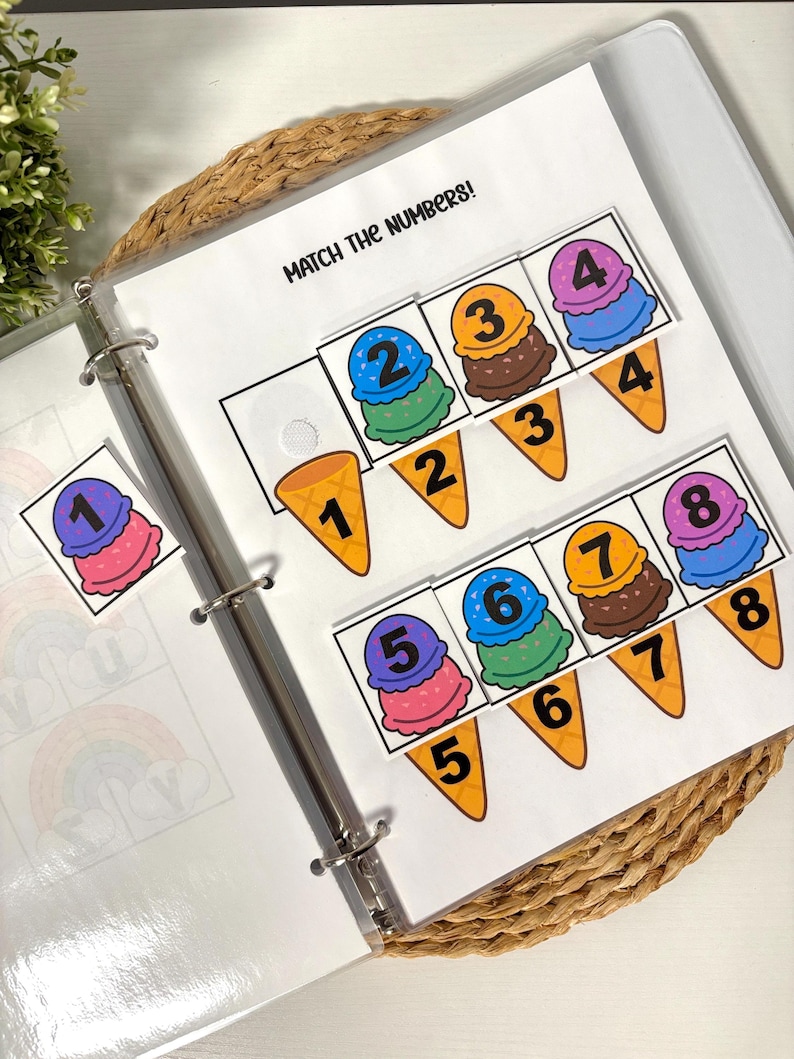 May include: A binder with pages featuring an ice cream-themed number matching game. The text "MATCH THE NUMBERS!" is at the top. Colorful ice cream scoops with numbers 1-8 are paired with matching cone shapes. The binder is on a woven mat.