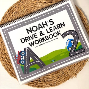 May include: A spiral-bound workbook titled "NOAH'S DRIVE & LEARN WORKBOOK" with a road design. The cover features a large letter "A" with a red truck and the number "2" with a blue car. The text reads "Learn A-Z AND 1-10 in a hands-on way!"
