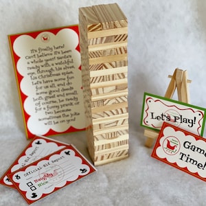 Könnte beinhalten: Ein Holz-Block-Stapelspiel mit einem roten und grünen Schild, auf dem "Let's Play!" steht, und einem roten Schild, auf dem "Game Time!" steht. Es gibt auch zwei rote und weiße Karten mit dem Text "Official Elf Report" und einer Checkliste für "Naughty" oder "Nice".