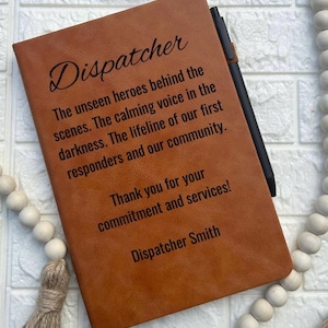 May include: A brown leather journal with the text "Dispatcher" and a quote about the importance of dispatchers. The quote reads: "The unseen heroes behind the scenes. The calming voice in the darkness. The lifeline of our first responders and our community. Thank you for your commitment and services!" The journal is signed "Dispatcher Smith".