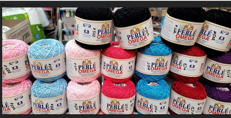 May include: A collection of colorful Perle Omega cotton yarn balls in various shades, including pink, blue, red, and black. Each ball is labeled with the brand name and product details. The yarn is suitable for crochet and embroidery projects.