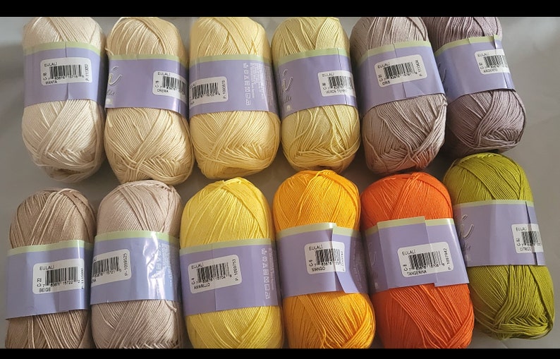 May include: A collection of yarn skeins in various colors, including cream, yellow, orange, and green. Each skein is wrapped with a purple label. The yarn is tightly wound, suggesting it's ready for knitting or crocheting projects.