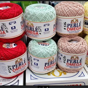 May include: A collection of Perle Omega cotton yarn balls in various colors, including red, beige, green, pink, yellow, and white. Each ball is labeled with the brand name and product information. Ideal for crochet and knitting projects.