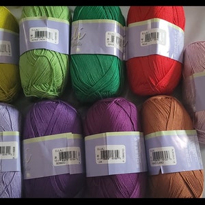 May include: A collection of colorful yarn skeins in various shades, including green, red, purple, and brown. Each skein is wrapped with a label. The yarn is likely for knitting or crocheting projects.