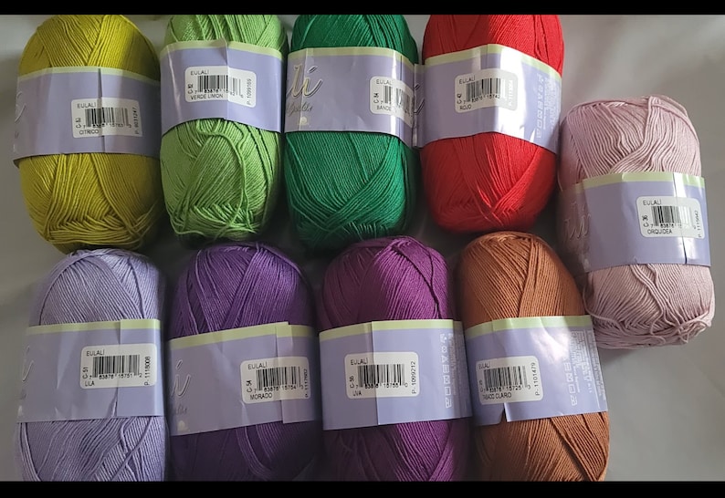 May include: A collection of colorful yarn skeins in various shades, including green, red, purple, and brown. Each skein is wrapped with a label. The yarn is likely for knitting or crocheting projects.