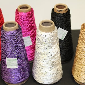 May include: Six spools of thread with sequins, in colours red, pink, purple, white, black, and gold. The spools are made of cardboard and have labels with the word "Angelique" on them.