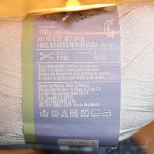 May include: A white yarn ball with a label wrapped around it. The label includes text indicating the yarn is 100% mercerized cotton, 100g, and 3.52 oz. It also has instructions and a brand logo.