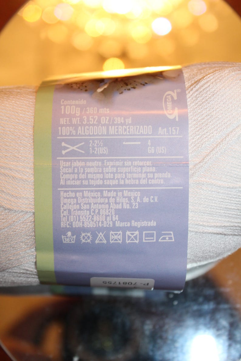 May include: A white yarn ball with a label wrapped around it. The label includes text indicating the yarn is 100% mercerized cotton, 100g, and 3.52 oz. It also has instructions and a brand logo.
