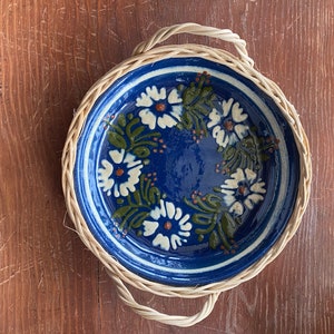 Puede incluir: Un plato de cerámica azul y blanco con un diseño floral, colocado en una cesta de mimbre tejida con asas.