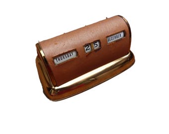 May include: A vintage desk calendar with a brown leatherette body and gold-toned metal accents. The calendar displays "Thursday" and "December 25" on rotating panels. A classic desk accessory.
