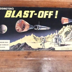 May include: A rectangular board game box titled Waddington's BLAST-OFF! featuring a space exploration theme. The black box cover displays a planet, spacecraft, an astronaut, and a lunar module on a rocky landscape with yellow text accents.