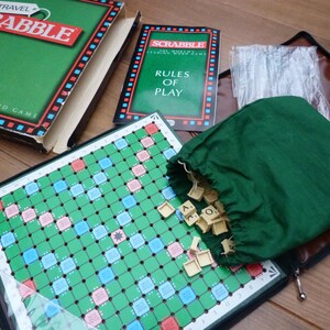 May include: A green travel Scrabble game with a green board, a green bag of tiles, and a set of rules. The game is in a brown case with a zipper.
