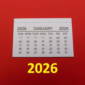 May include: A white rectangular calendar page for January 2026 with black text and numbers. The header displays the year 2026 on both sides of the month name. Below, the days of the week are listed with dates from 01 to 31. The number 2026 is printed in large yellow font below the calendar.