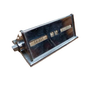 May include: A vintage chrome desk calendar displaying "Friday" and "December 25". The calendar has a rectangular shape with a rotating mechanism on the side. The date is displayed in a clear, easy-to-read font.