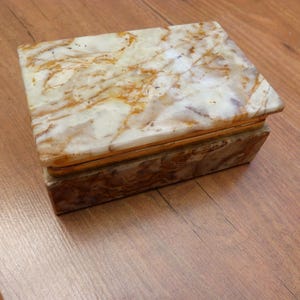 May include: A white and brown marble jewellery box with a hinged lid. The box has a decorative pattern on the top and bottom.