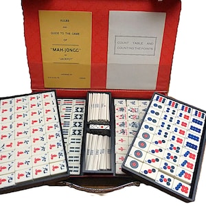 Peut inclure: Un jeu de Mah-Jong dans une mallette rouge contenant des tuiles blanches avec des symboles rouges, bleus et noirs. Le coffret comprend deux livrets d'instructions intitul&eacute;s Rules and Guide to the Game of Mah-Jongg by Jackpot et Count Table.