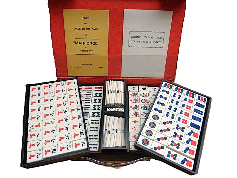 Peut inclure: Un jeu de Mah-Jong dans une mallette rouge contenant des tuiles blanches avec des symboles rouges, bleus et noirs. Le coffret comprend deux livrets d'instructions intitul&eacute;s Rules and Guide to the Game of Mah-Jongg by Jackpot et Count Table.