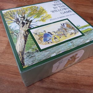 Könnte beinhalten: Ein Brettspiel in einer Box mit dem Titel "The Wind in the Willows Game". Die grüne und weiße Box zeigt Illustrationen von Charakteren und Szenen aus der Geschichte, mit einem Baum und einer Flussszene.