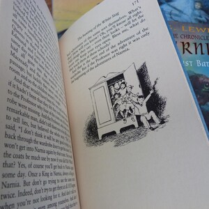 May include: A close-up of a book page with black and white illustrations of children entering a wardrobe. The text on the page reads "The hunting of the White Stag" and "Bless me, what do you know? Oh, you'll know all right. Children will say their eyes open... But if the Professor was right it was only the beginning of the adventures of Narnia."