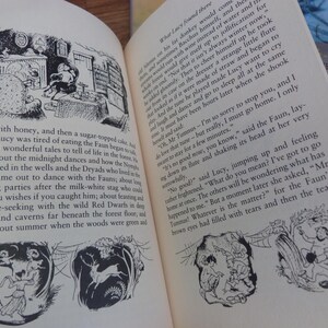 May include: Black and white illustration of a scene from a children's book. The illustration shows a faun playing a flute, a girl sitting on a chair, and a fireplace. The text in the image reads "What Lucy found there..."