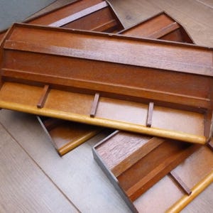 May include: A collection of wooden shelves in various shades of brown are displayed on a light wooden surface. Each shelf has a rectangular design with a curved front edge and small vertical supports.