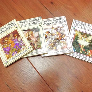 May include: Four hardback books titled Flower Fairies of the Spring, The Summer, The Autumn, and Of the Winter by Cicely Mary Barker. Each book cover features a colour illustration of a fairy surrounded by seasonal flora and decorative borders.