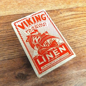 May include: A rectangular deck of Viking Playing Cards with a white background and red ink graphics. The box features a stylized Viking ship illustration, the text VIKING PLAYING CARDS, LINEN FINISH, and JOHN WADDINGTON LTD. LEEDS & LONDON.