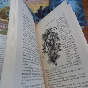 May include: A close-up of a page from a book with a black and white illustration of a creature with a bird's head and a long, thin body. The text on the page reads "He was brave enough in battle; but half his courage had left him earlier that night when he first began to suspect there might be a real Tash. The rest of it had left him now."