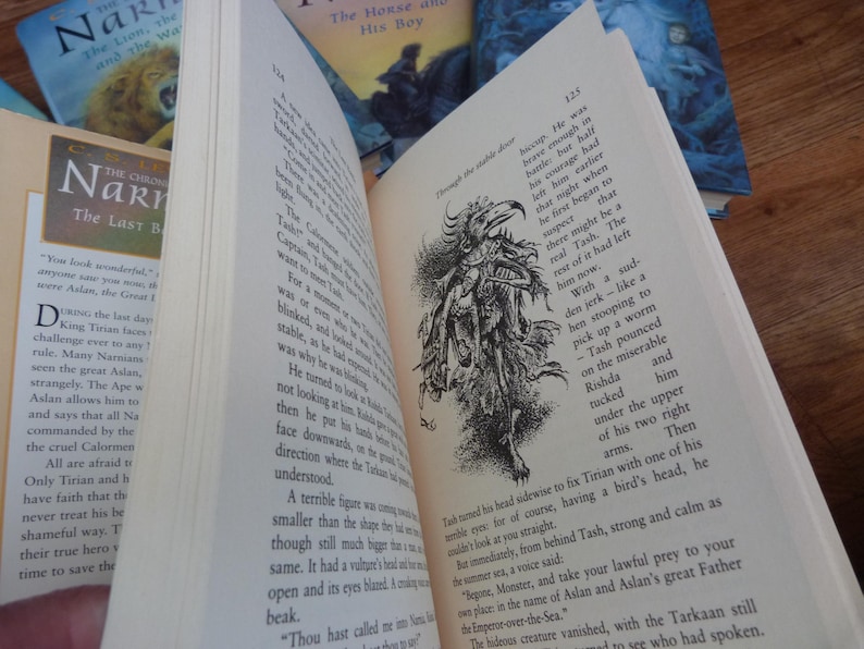 May include: A close-up of a page from a book with a black and white illustration of a creature with a bird's head and a long, thin body. The text on the page reads "He was brave enough in battle; but half his courage had left him earlier that night when he first began to suspect there might be a real Tash. The rest of it had left him now."