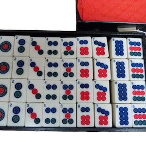 Peut inclure: Un plateau rectangulaire noir contenant un ensemble de tuiles de mah-jong blanc cass&eacute; dispos&eacute;es en quatre rang&eacute;es. Chaque tuile pr&eacute;sente un chiffre de un &agrave; neuf, repr&eacute;sent&eacute; par des motifs circulaires rouges, bleus et verts. Les tuiles sont lisses.