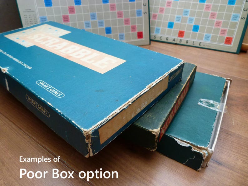 Puede incluir: Primer plano de tres cajas de juego azules y verdes apiladas una encima de la otra. La caja superior tiene la palabra "SCRABBLE" impresa en blanco en la parte delantera. Las cajas est&aacute;n desgastadas y muestran signos de edad.