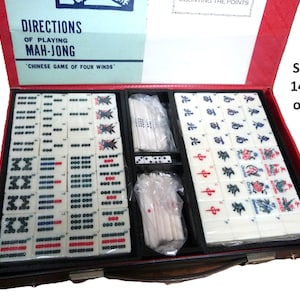 Peut inclure: Un jeu de Mah-Jong dans un coffret rouge avec un couvercle portant le texte DIRECTIONS OF PLAYING MAH-JONG CHINESE GAME OF FOUR WINDS. L'int&eacute;rieur contient 144 tuiles blanches avec divers symboles, caract&egrave;res et couleurs, ainsi que des b&acirc;tonnets et d&eacute;s.