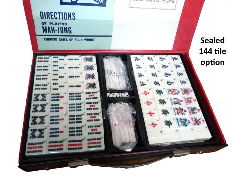 Peut inclure: Un jeu de Mah-Jong dans un coffret rouge avec un couvercle portant le texte DIRECTIONS OF PLAYING MAH-JONG CHINESE GAME OF FOUR WINDS. L'int&eacute;rieur contient 144 tuiles blanches avec divers symboles, caract&egrave;res et couleurs, ainsi que des b&acirc;tonnets et d&eacute;s.