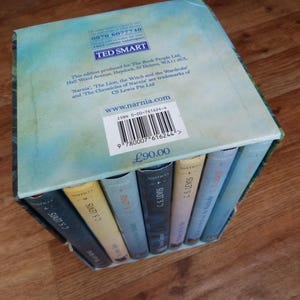 May include: A boxed set of seven books, The Chronicles of Narnia by C.S. Lewis. The box is blue and green with a white label that says "www.narnia.com". The books are stacked on top of each other and have a blue and white cover with the author's name on the spine.
