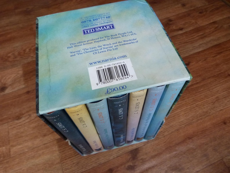 May include: A boxed set of seven books, The Chronicles of Narnia by C.S. Lewis. The box is blue and green with a white label that says "www.narnia.com". The books are stacked on top of each other and have a blue and white cover with the author's name on the spine.