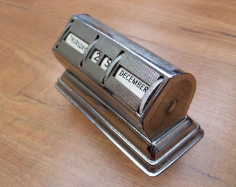 May include: A silver desktop calendar with a black base. The calendar displays the date "25 December" and the day of the week "Thursday".